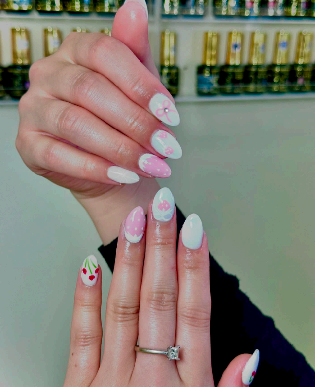 A hand with bow and floral nail art held against the studio's wall of polish bottles